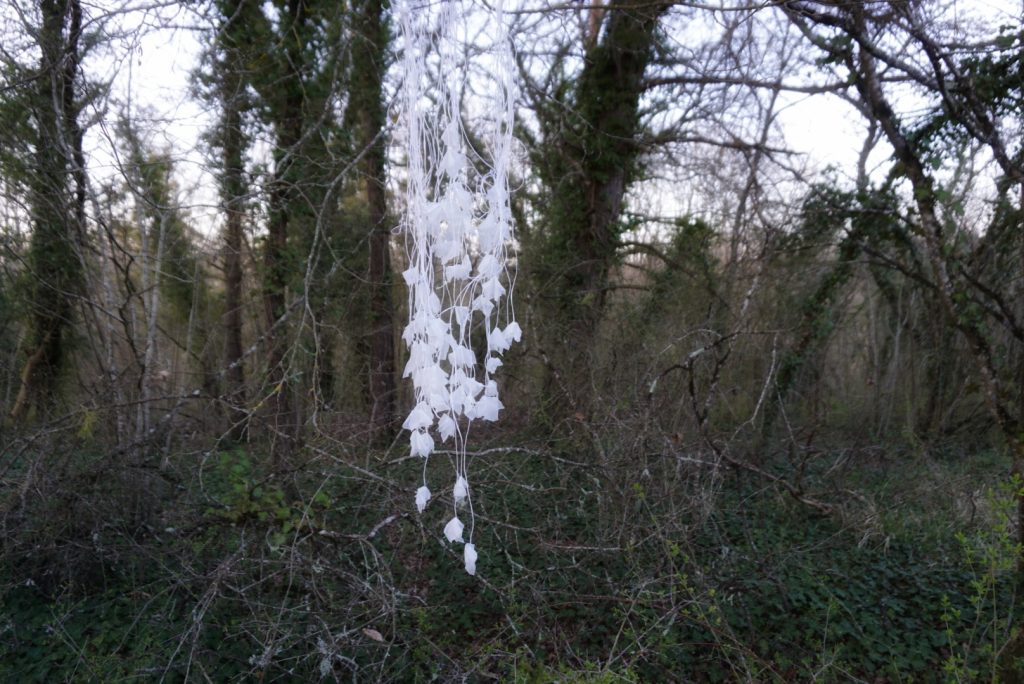 Sculpture en papier calque et ficelle blanche accrochée dans les arbres