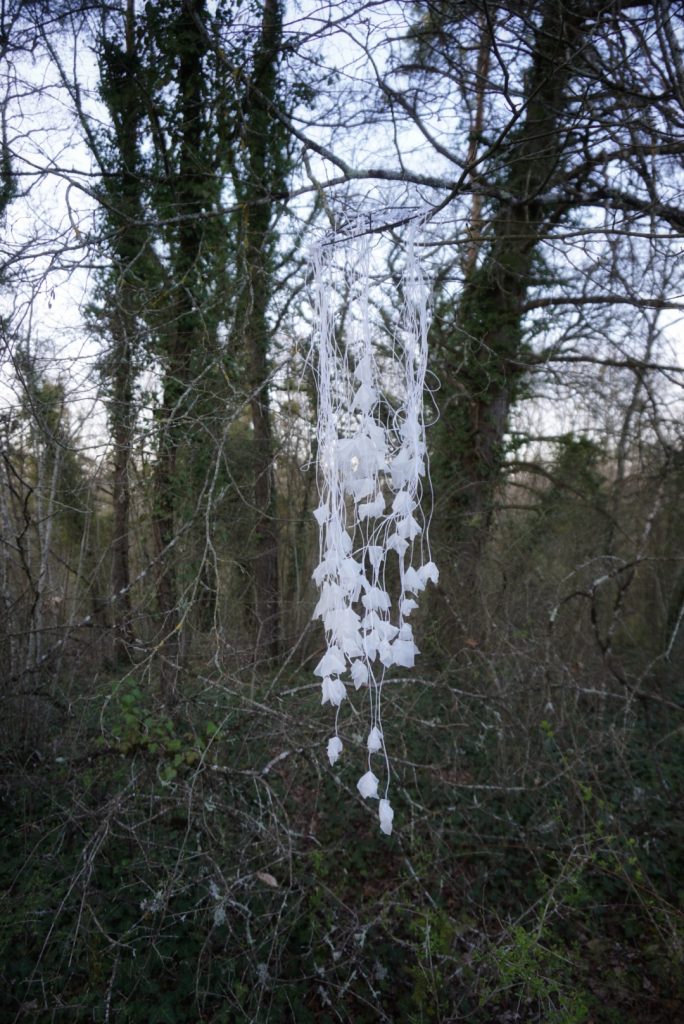 Sculpture en papier calque et ficelle blanche accrochée dans les arbres