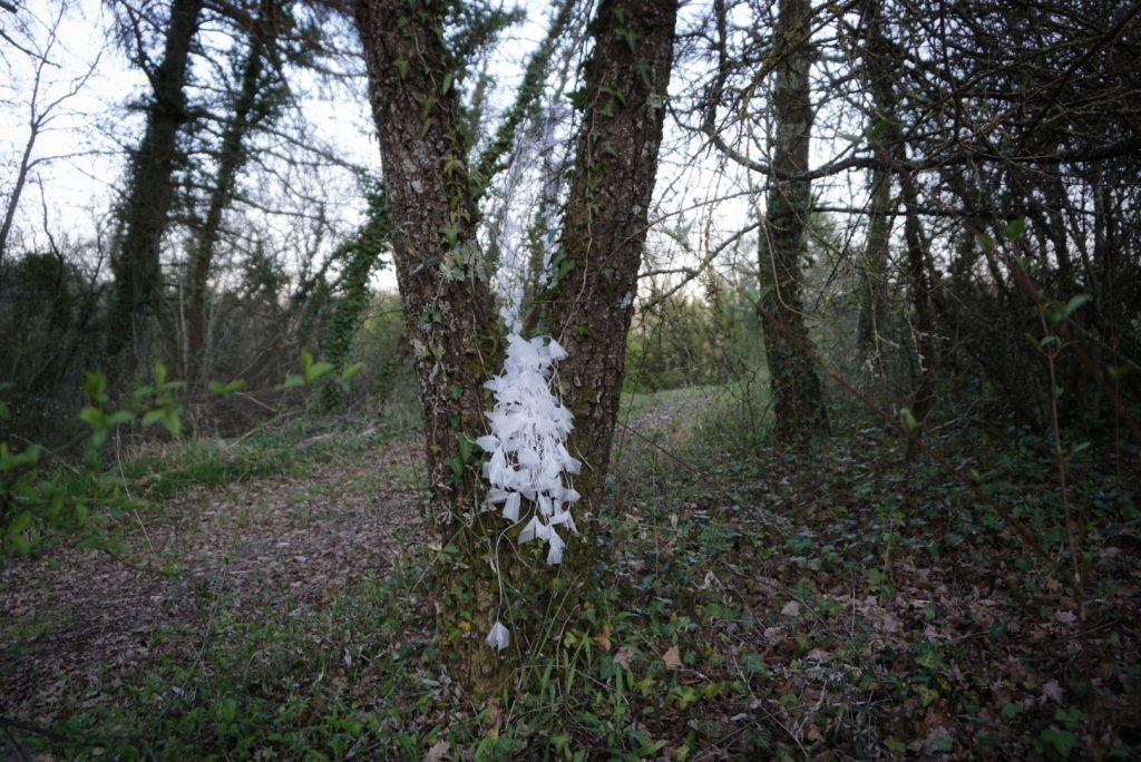 Sculpture en papier calque et ficelle blanche accrochée dans les arbres