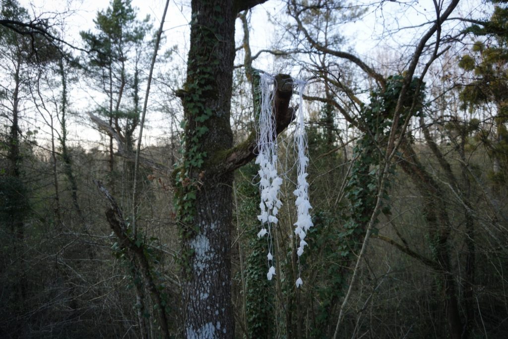 Sculpture en papier calque et ficelle blanche accrochée dans les arbres