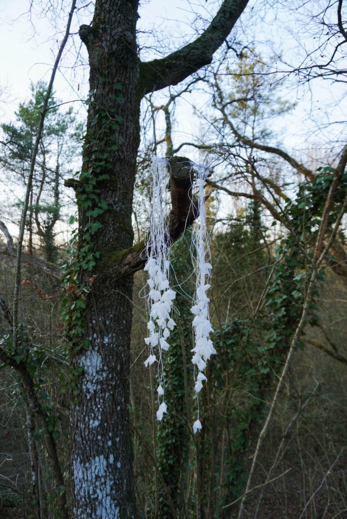 Sculpture en papier calque et ficelle blanche accrochée dans les arbres