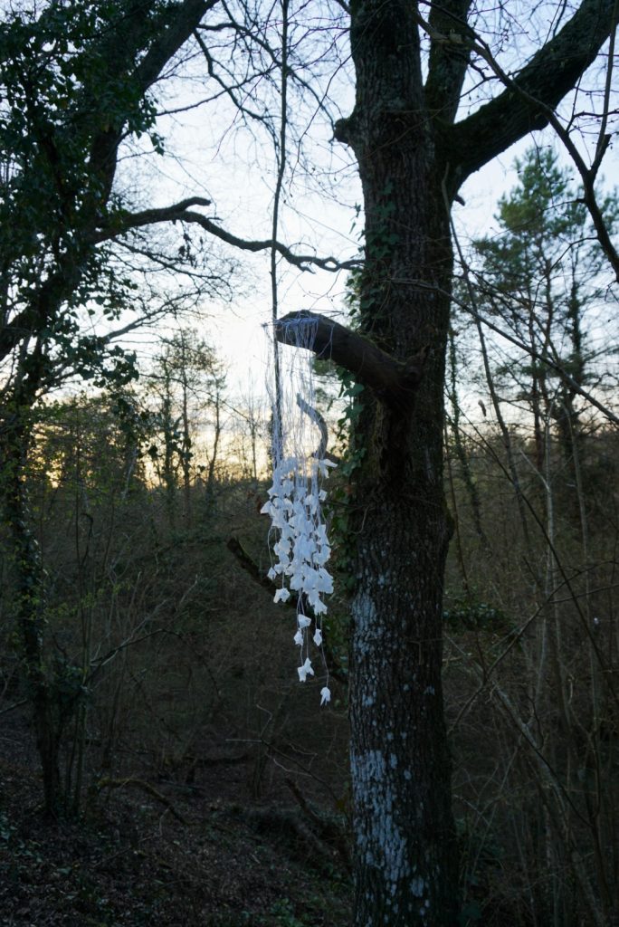 Sculpture en papier calque et ficelle blanche accrochée dans les arbres