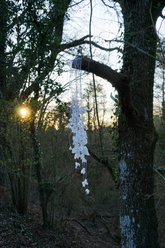 Sculpture en papier calque et ficelle blanche accrochée dans les arbres