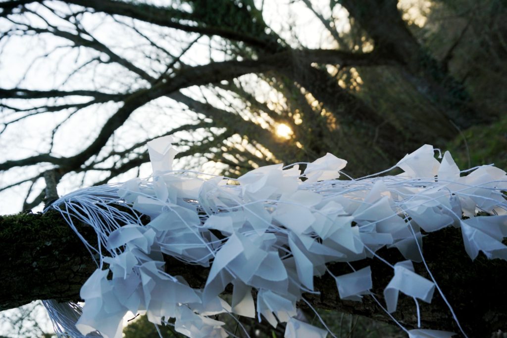Sculpture en papier calque et ficelle blanche accrochée dans les arbres