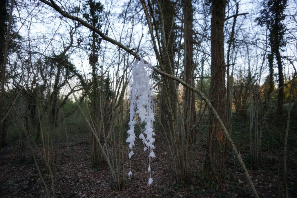 Sculpture en papier calque et ficelle blanche accrochée dans les arbres