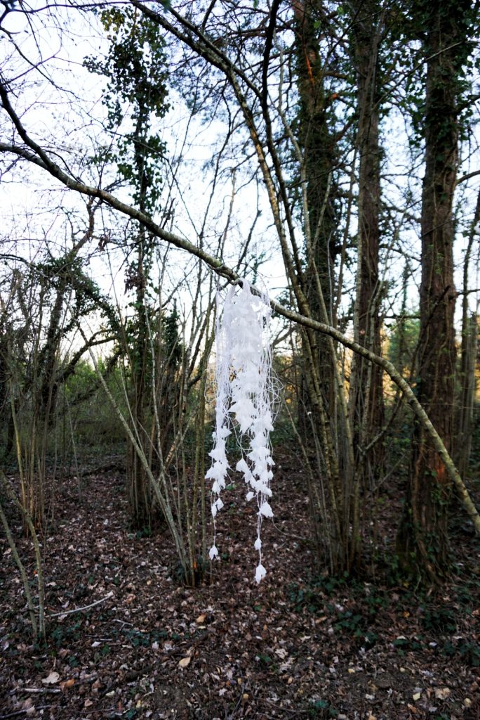 Sculpture en papier calque et ficelle blanche accrochée dans les arbres