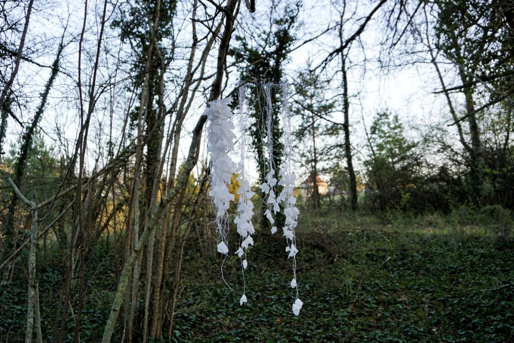 Sculpture en papier calque et ficelle blanche accrochée dans les arbres