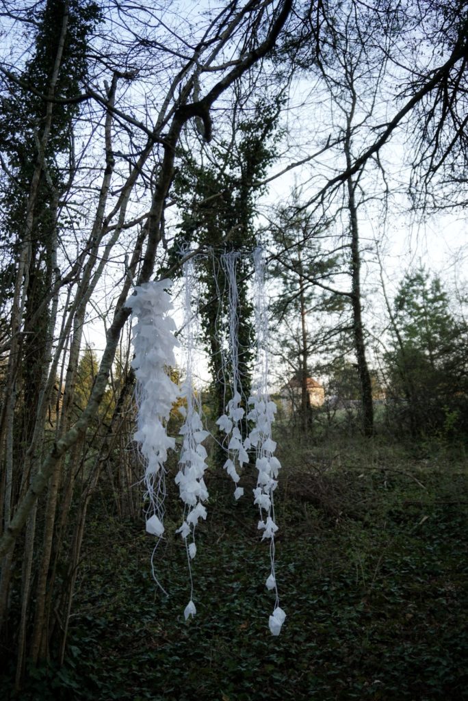 Sculpture en papier calque et ficelle blanche accrochée dans les arbres