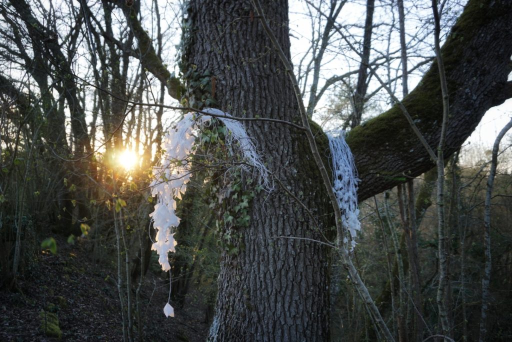 Sculpture en papier calque et ficelle blanche accrochée dans les arbres