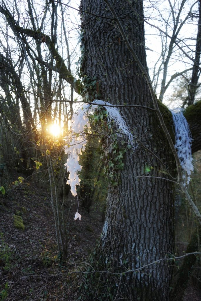 Sculpture en papier calque et ficelle blanche accrochée dans les arbres