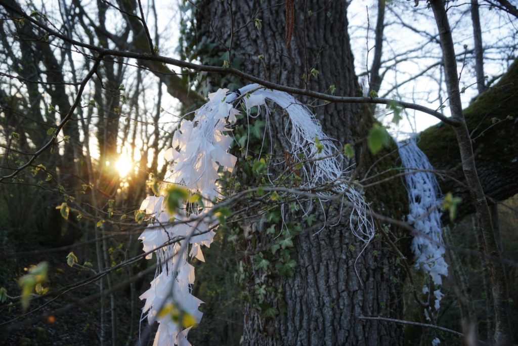 Sculpture en papier calque et ficelle blanche accrochée dans les arbres