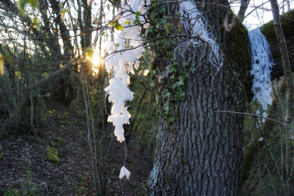 Sculpture en papier calque et ficelle blanche accrochée dans les arbres