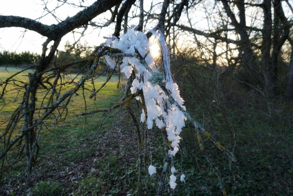 Sculpture en papier calque et ficelle blanche accrochée dans les arbres