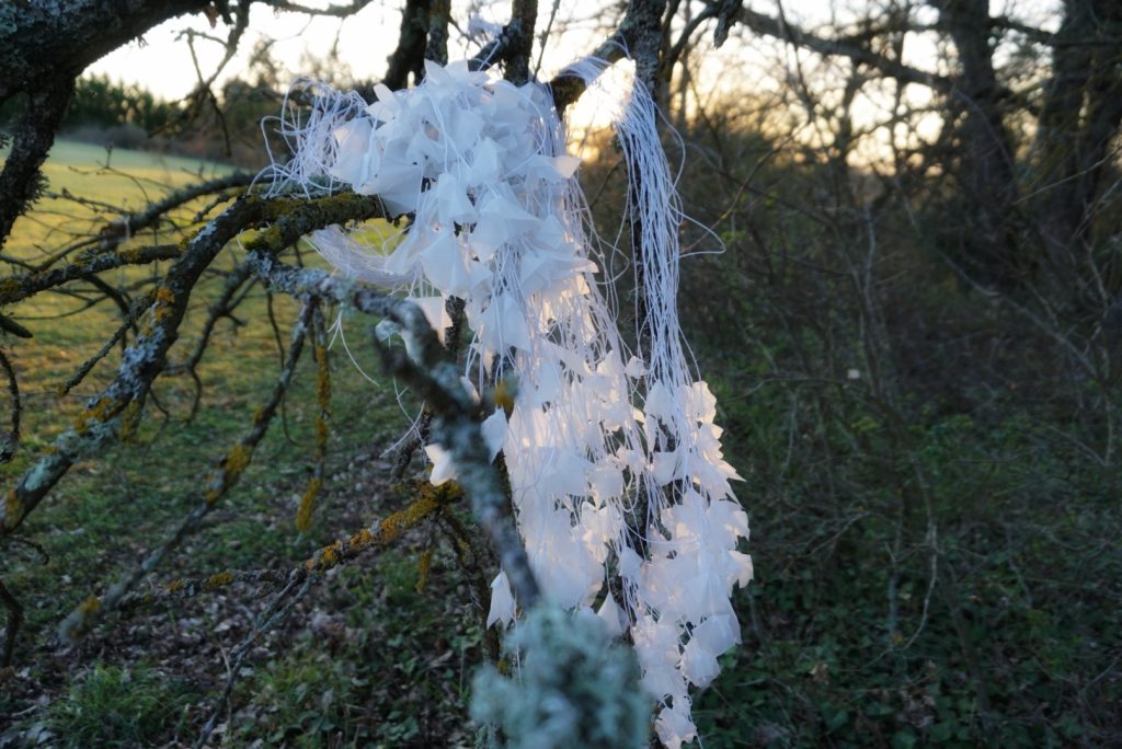 Sculpture en papier calque et ficelle blanche accrochée dans les arbres