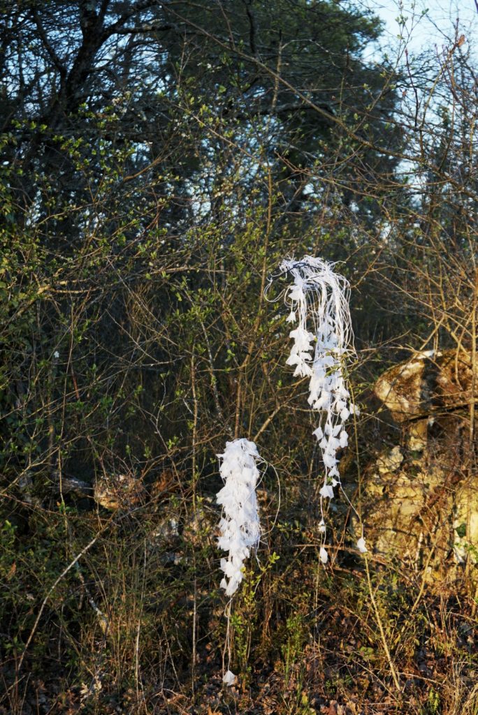 Sculpture en papier calque et ficelle blanche accrochée dans les arbres