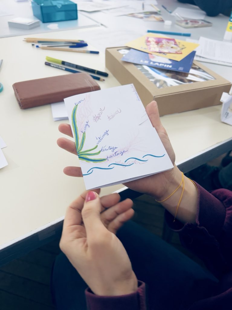 Photo, photographie d’une participante dont on voit seulement la main qui montre ce qu’elle a produit sur son papier blanc