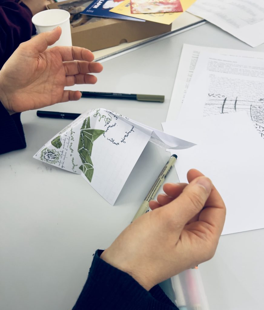 Photo, photographie d’une participante dont on voit seulement la main qui montre ce qu’elle a produit sur son papier blanc